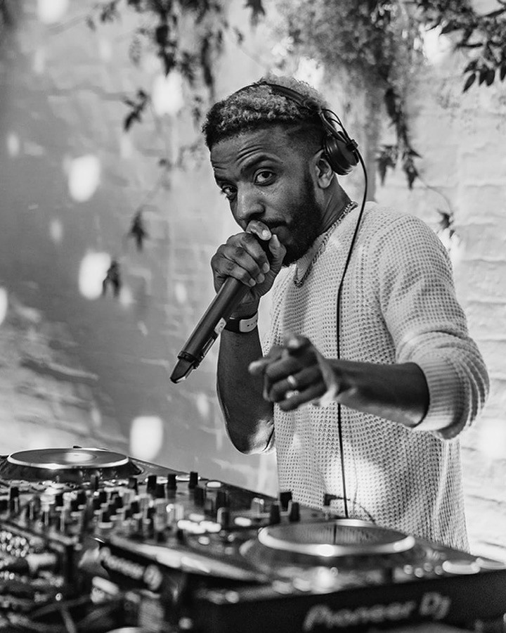 DJ T-Russ performing at the decks with a microphone
